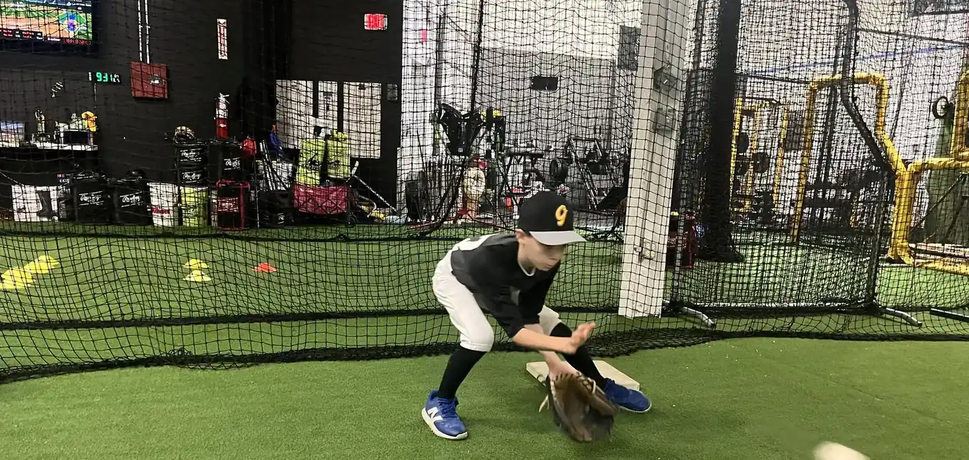 A young player fielding a ground ball on the turf inside the Gorilla facility