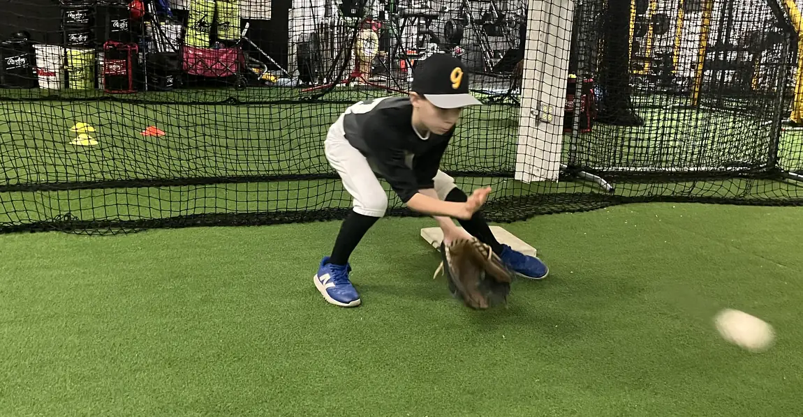 A young player fielding a ground ball on the turf inside the Gorilla facility