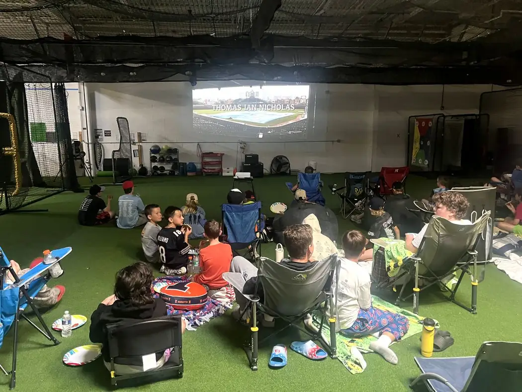 Gorilla players sitting on the turf watching a movie projected on the facility wall